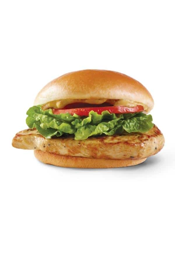 A grilled chicken sandwich with lettuce, tomato, and mustard.