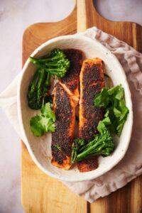 two blackened salmon fillets in a deep white dish garnished with cilantro and seared broccolini.