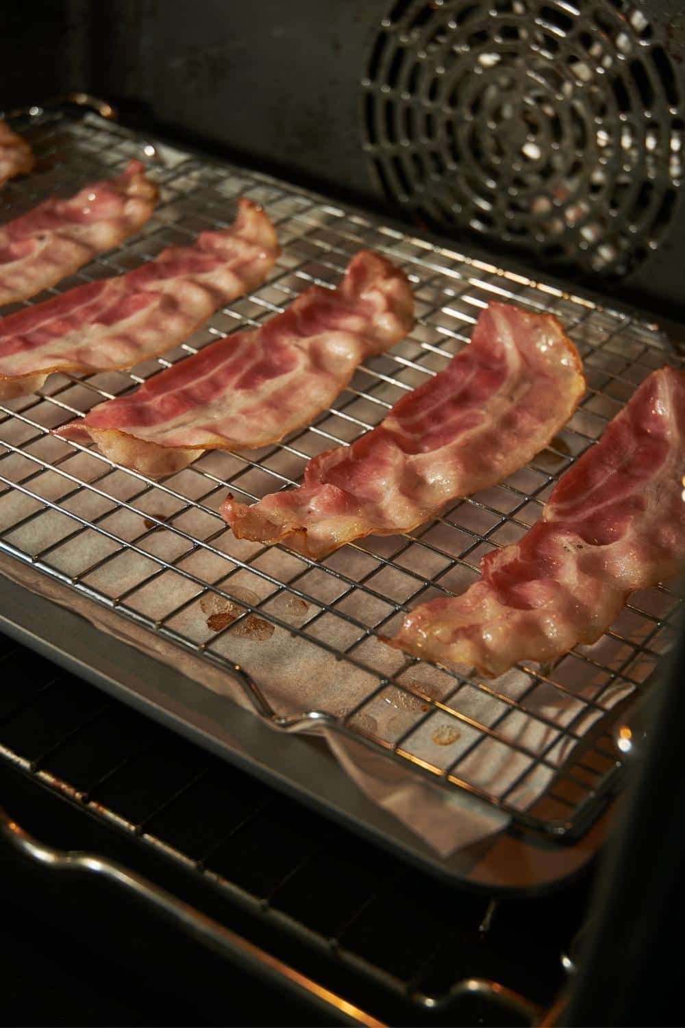 Half-cooked turkey bacon slices on a baking rack in the oven. A baking sheet lined with parchment paper sits under the rack, catching any extra bacon fat.