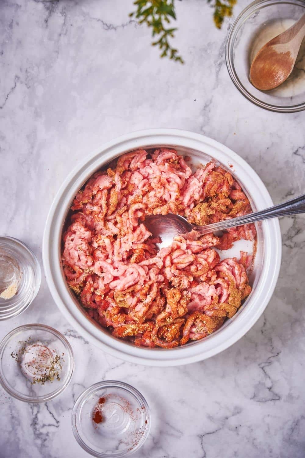 Raw ground pork being mixed with seasonings in a large bowl with a spoon. W