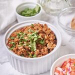 Close up shot of a bowl of chorizo garnished with chopped cilantro. The chorizo is golden brown with crispy bits. To the side is a small bowl of salsa and a smaller bowl of cilantro.