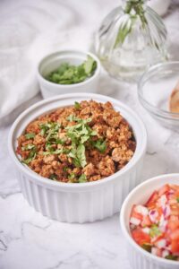 Close up shot of a bowl of chorizo garnished with chopped cilantro. The chorizo is golden brown with crispy bits. To the side is a small bowl of salsa and a smaller bowl of cilantro.