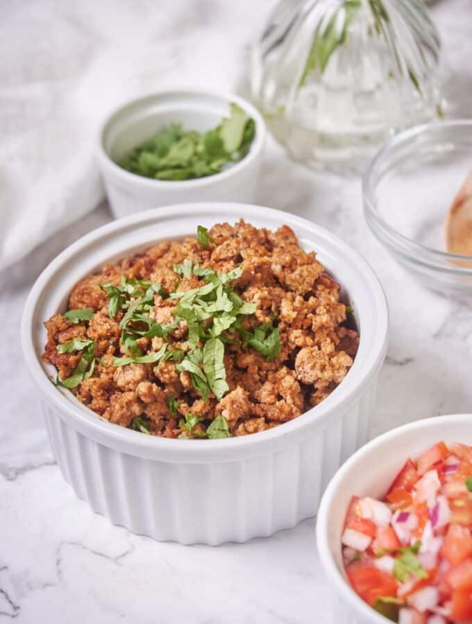 Close up shot of a bowl of chorizo garnished with chopped cilantro. The chorizo is golden brown with crispy bits. To the side is a small bowl of salsa and a smaller bowl of cilantro.