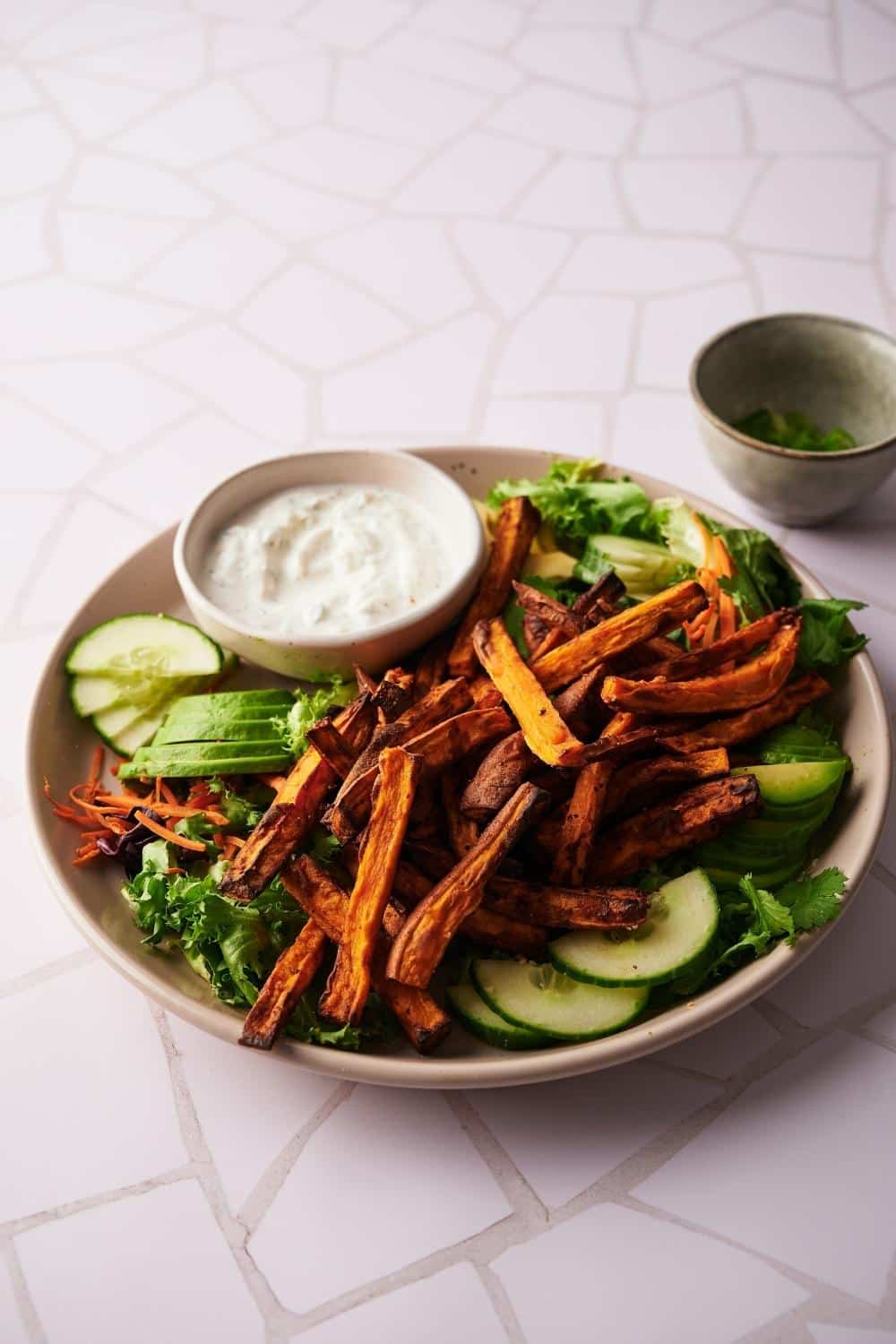 Air fried sweet potato fries on a bed of lettuce and cucumber slices with a small bowl of creamy dipping sauce.