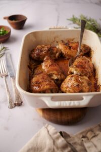 a spoon taking out a chicken thigh from a tray of baked chicken thighs