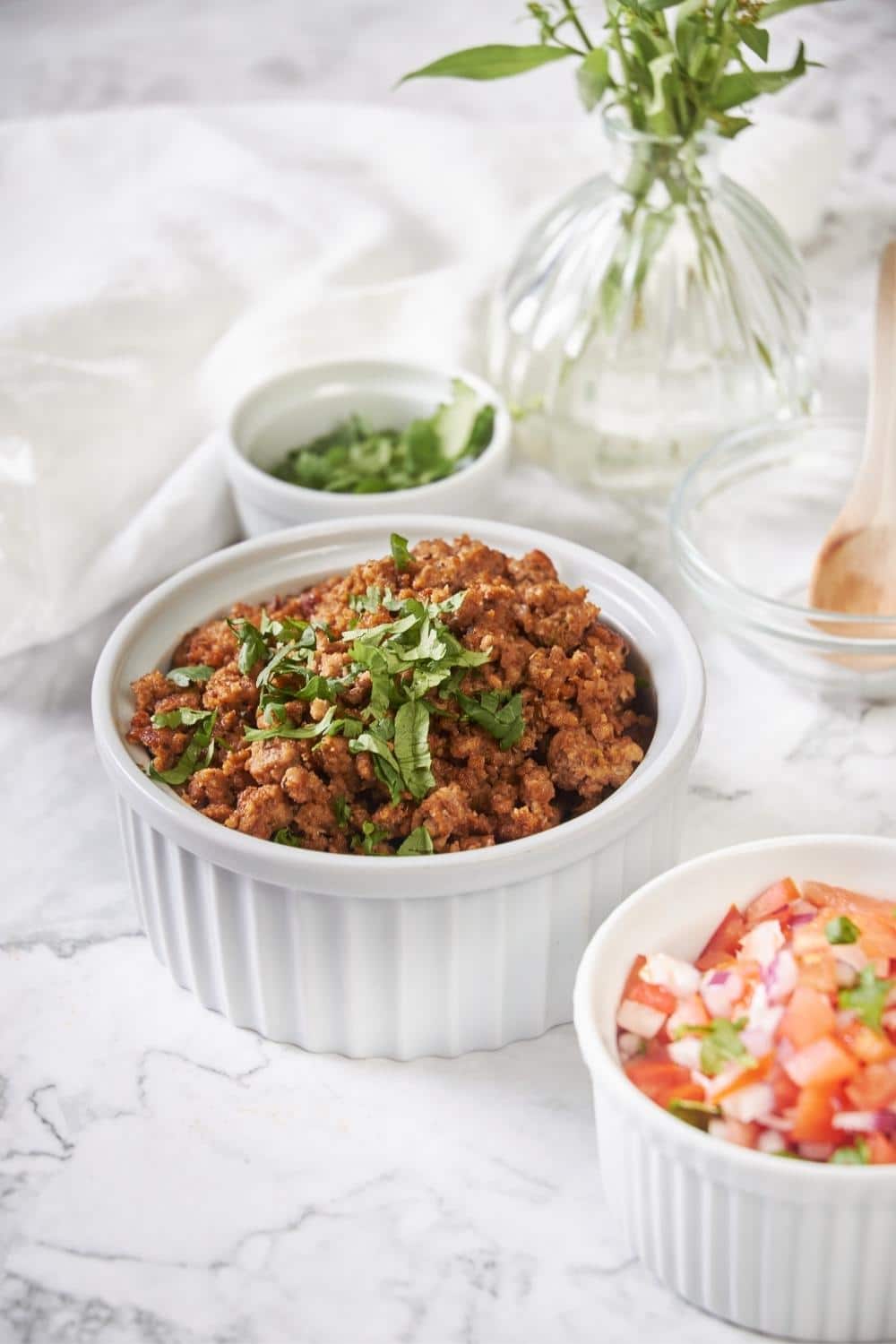 A bowl of cooked chorizo crumbles next to smaller bowls of fresh tomato salsa and chopped cilantro.