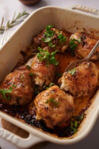 close up shot of a spoon taking a baked chicken thigh out of a tray of 6 baked chicken thighs