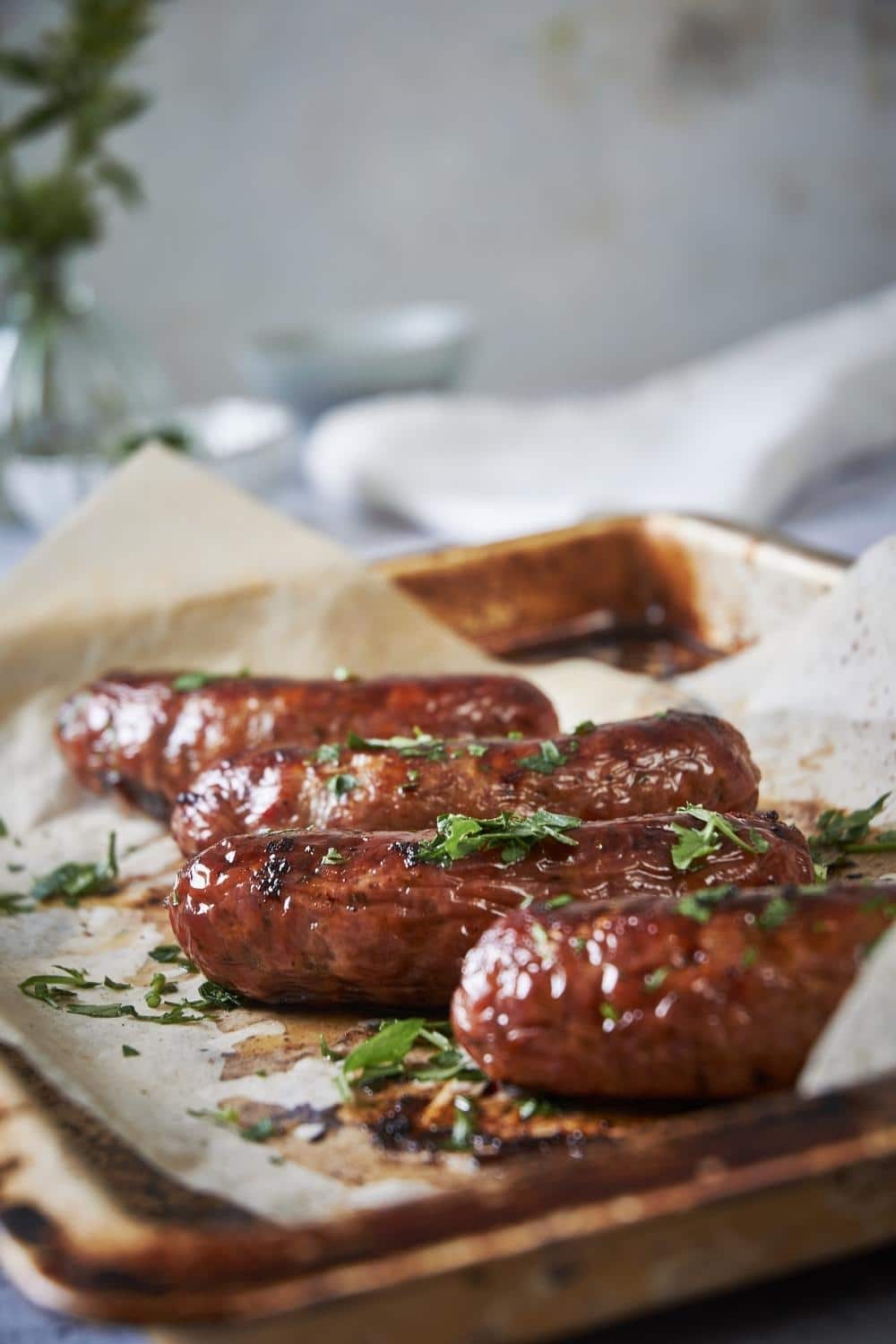 Four roasted brats garnished with parsley in a sheet pan lined with parchment paper.