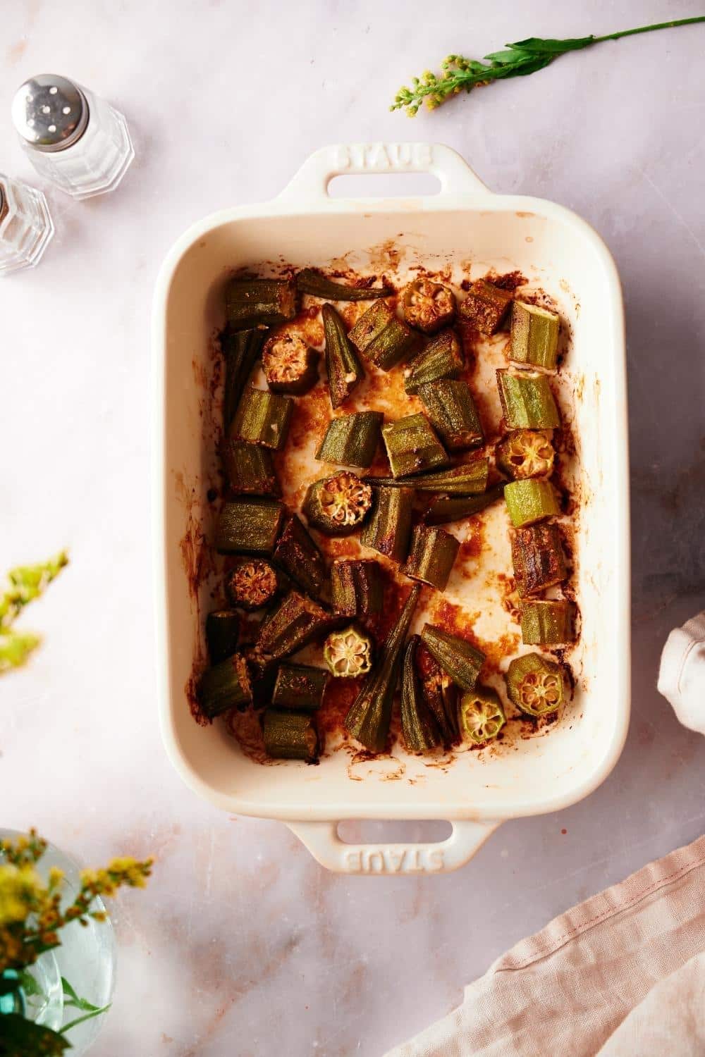 top view of garlic roasted okra in a white baking tray on a marble countertop.