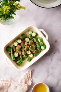 chopped okra pieces coated in seasoning in a white Staub baking dish on a marble countertop.