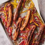 Roasted chicken sausages, bell peppers, and onions on a parchment paper lined baking tray.