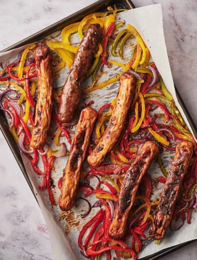 Roasted chicken sausages, bell peppers, and onions on a parchment paper lined baking tray.