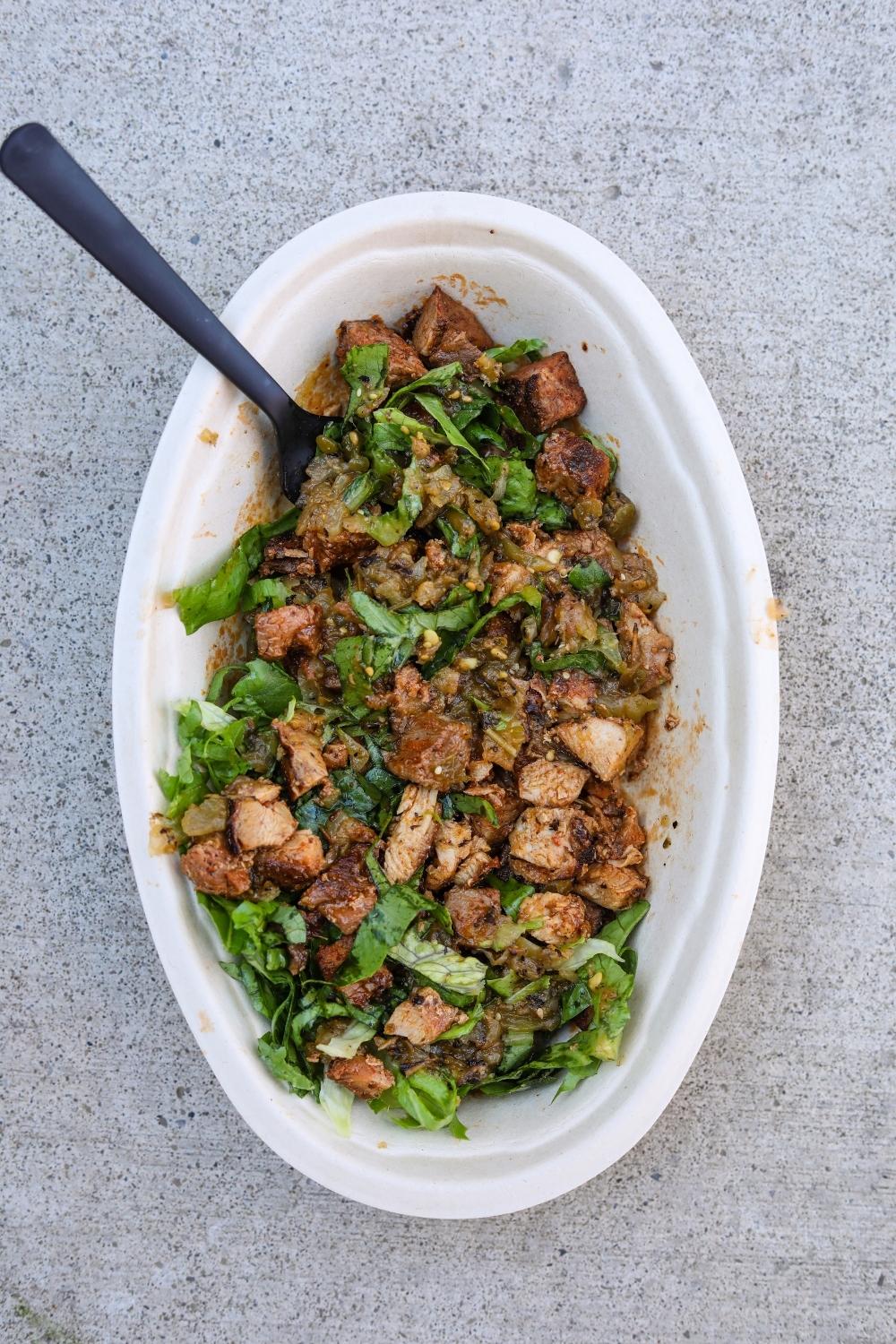 Chicken, green salsa, and shredded lettuce in an oval white bowl.