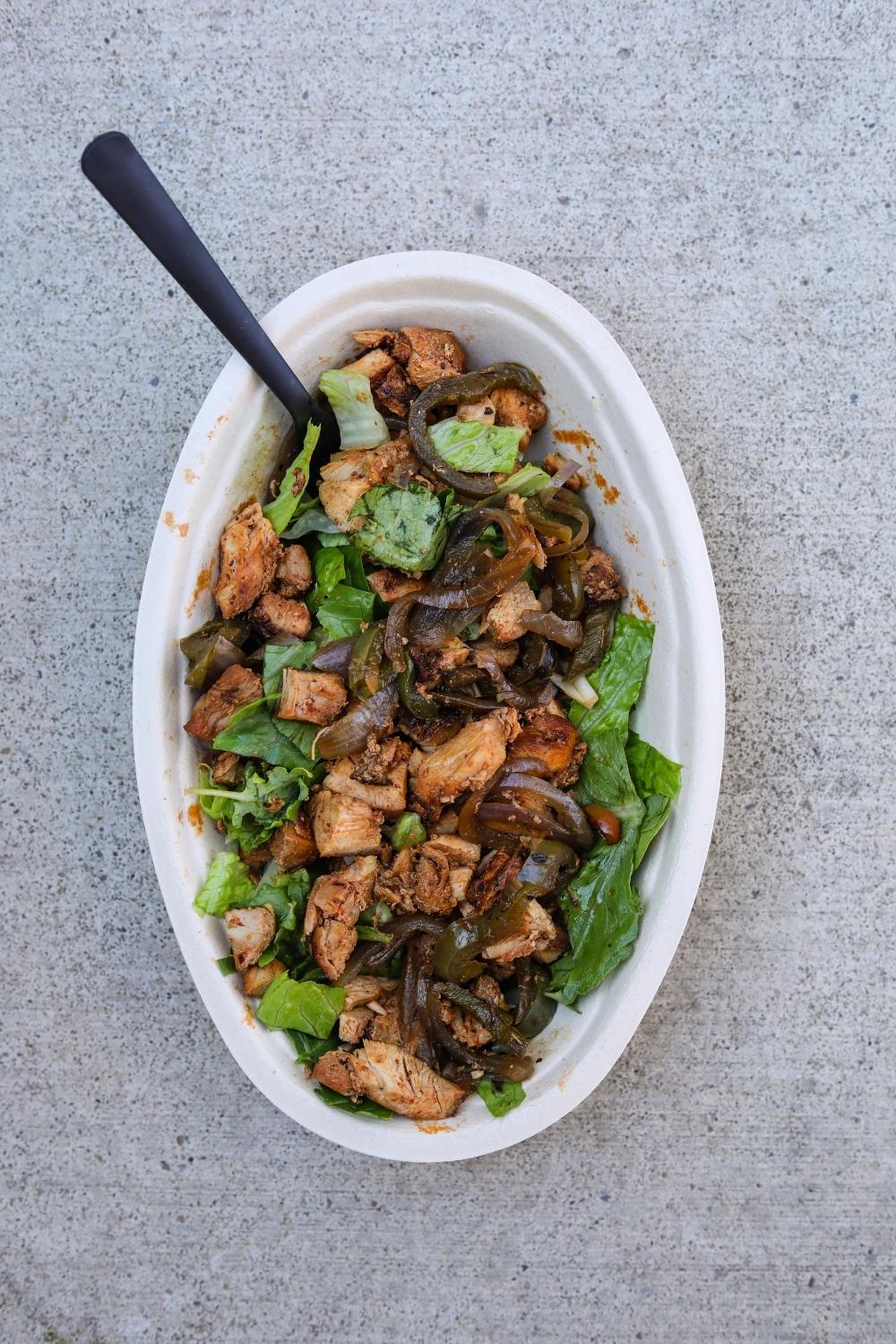 Chicken, fajita veggies, and lettuce in an oval white bowl.