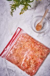 Raw chorizo flattened in a zip lock bag. A wooden spoon rests on a small glass bowl next to the chorizo.