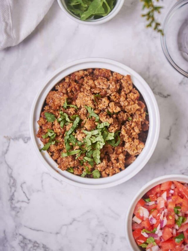 Top shot of a bowl of cooked chorizo next to a bowl of fresh salsa and a bowl of cilantro. The chorizo is garnished with cilantro.