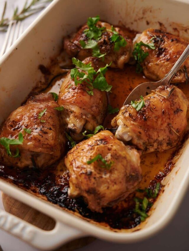 close up shot of a spoon taking a baked chicken thigh out of a tray of 6 baked chicken thighs