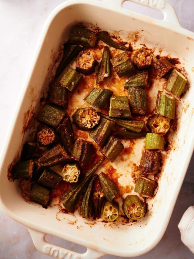 close up of cooked roasted okra in a white baking dish on a white marble countertop.
