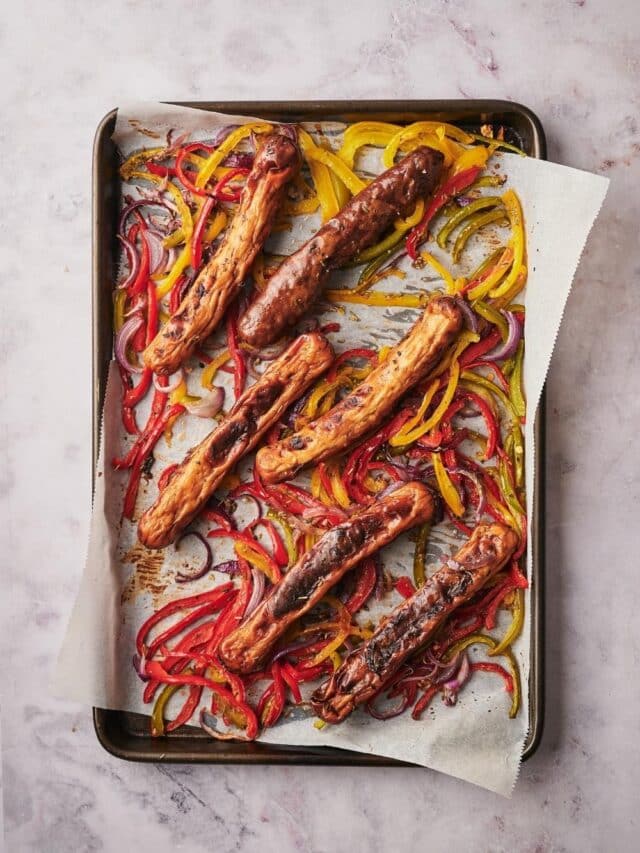 Roasted chicken sausages, bell peppers, and onions on a parchment paper lined baking tray