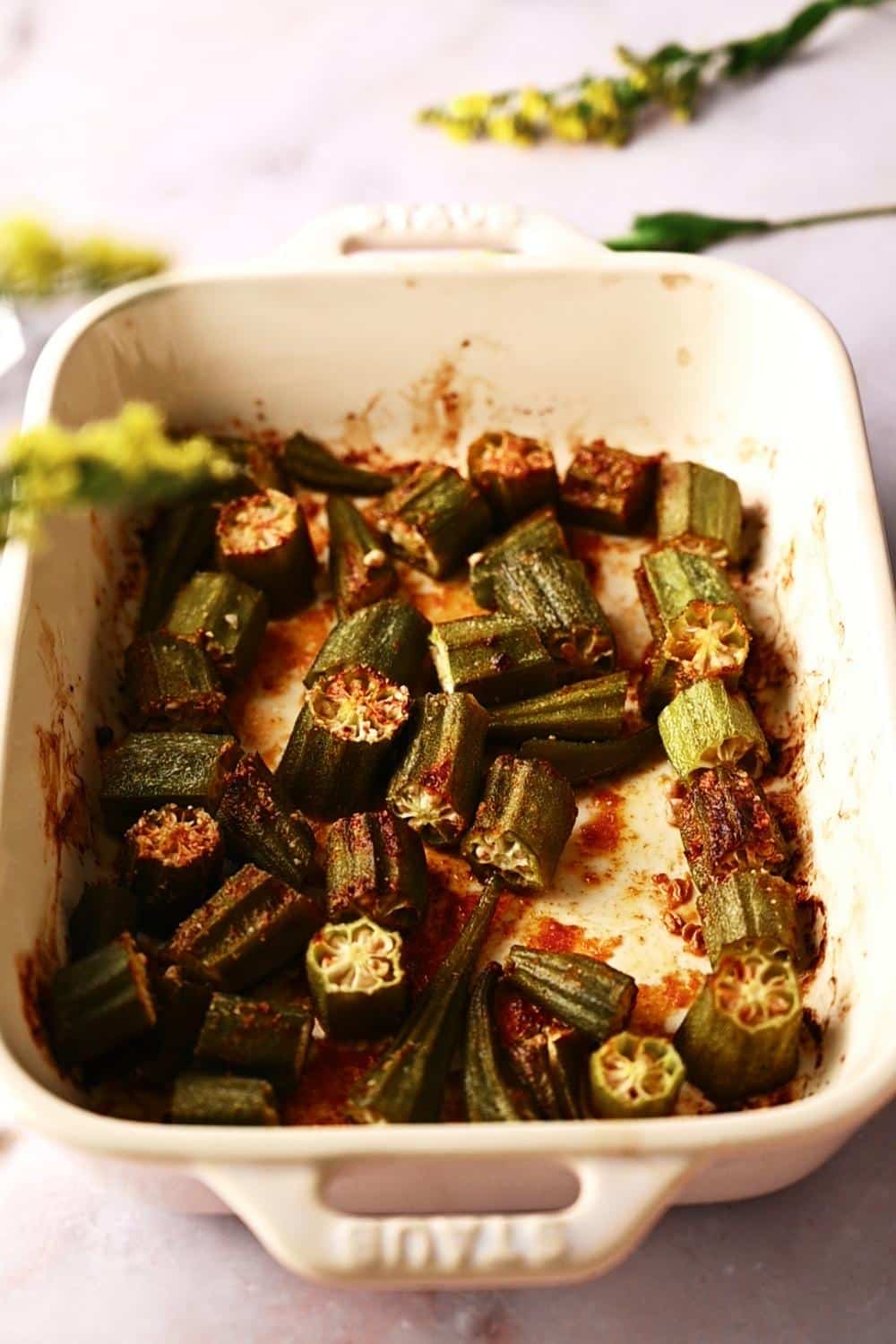 close up shot of freshly made oven roasted okra in a white baking dish on a marble countertop