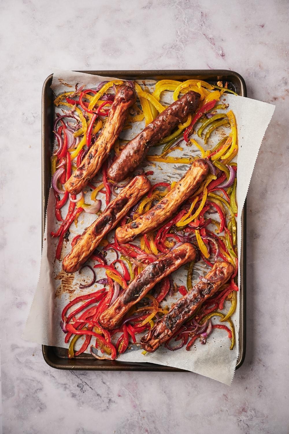 Roasted chicken sausages, bell peppers, and onions on a parchment paper lined baking tray