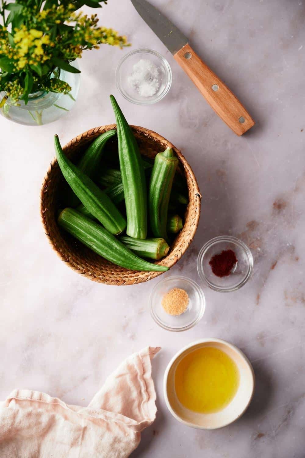 a bowl of whole okra pods next to small bowls of salt, garlic powder, paprika, and melted butter