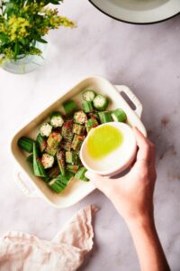 Melted butter being poured over seasoned chopped okra in a white baking dish