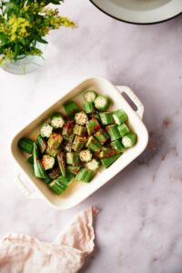 chopped okra in a white baking dish. The pieces are coated in seasoning and melted butter.