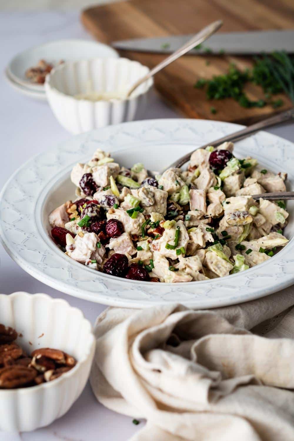 A white bowl with turkey salad and utensils in it.