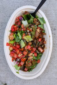 Fresh tomato salsa on top of lettuce with chicken in an oval white bowl.