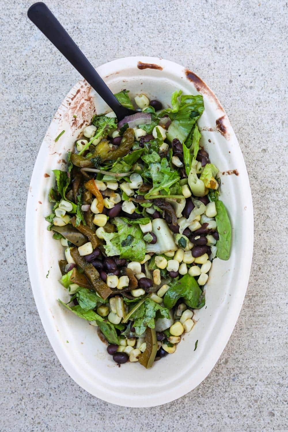 Corn, lettuce, fajita veggies, and black beans in a white oval bowl.