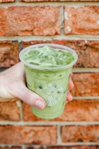 A hand holding a clear cup of Starbucks iced matcha green tea latte.