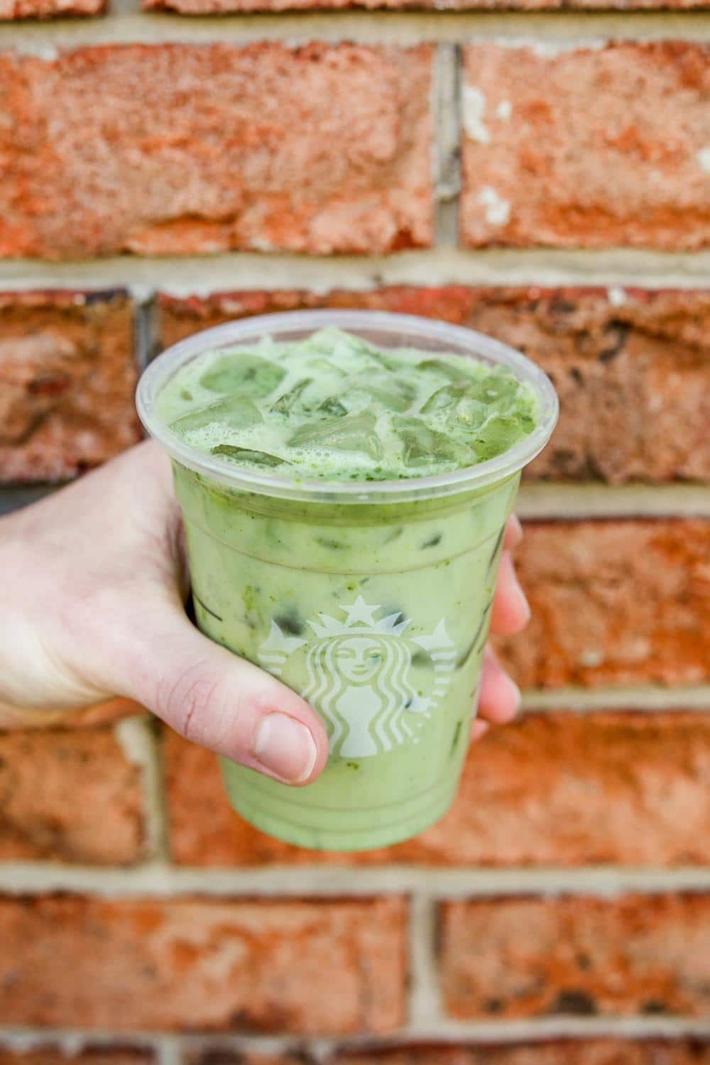 A hand holding a clear cup of Starbucks iced matcha green tea latte.