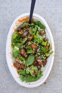 Lettuce, steak, and rice in an oval white bowl.