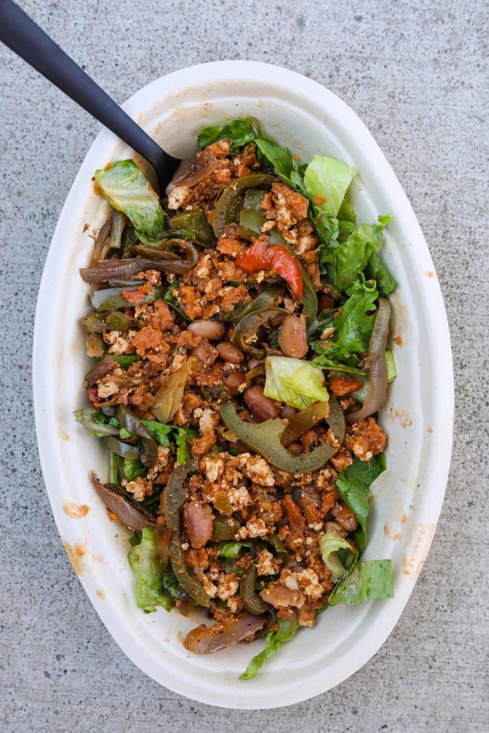 Sofritas, fajita veggies, and lettuce in an oval white bowl.