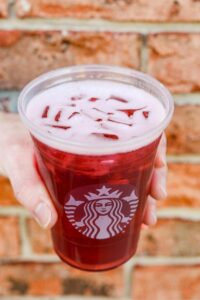 A hand holding a clear cup of Starbucks iced passion tango tea.