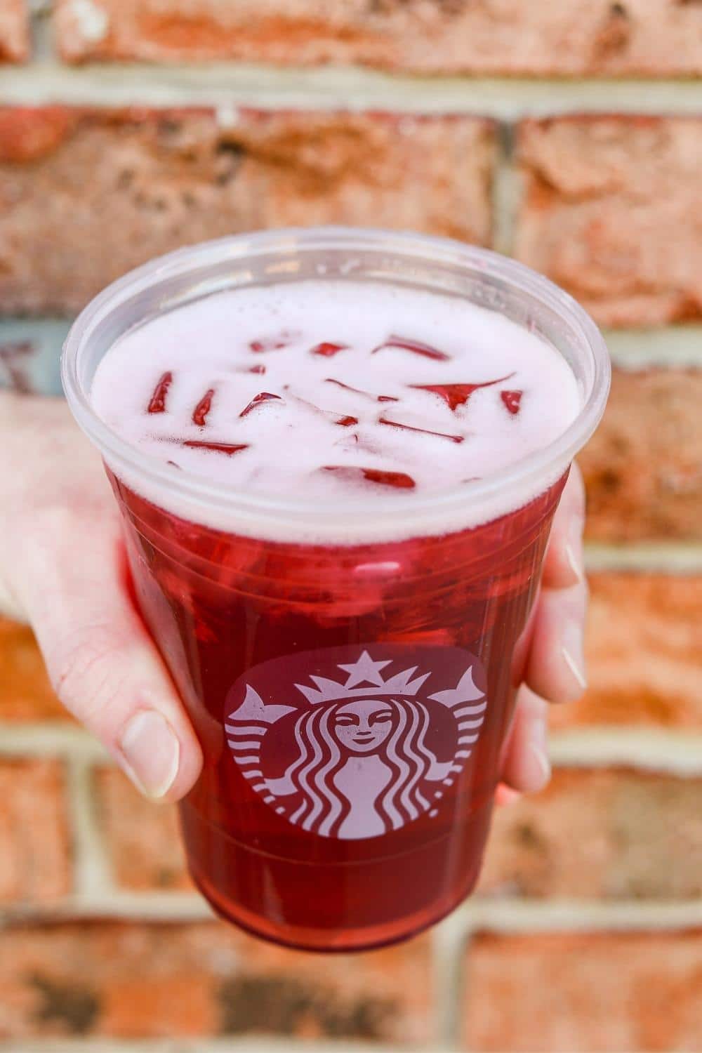 A hand holding a clear cup of Starbucks iced passion tango tea.