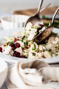 Two spoons picking up turkey salad out of a bowl that is filled with the turkey salad.