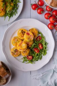 A bunch of egg bites next to arugula and tomatoes on a plate.