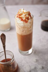 Keto frappuccino in a tall skinny glass topped with whipped cream and caramel sauce.