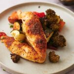 Two pieces of chicken on top of roasted cucumber, broccoli, and carrots.