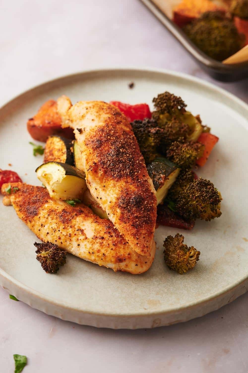 Two pieces of chicken on top of roasted cucumber, broccoli, and carrots.