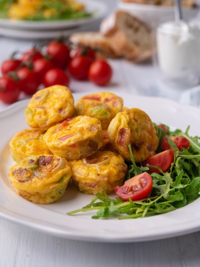 Several egg bites on top of one another on a plate with arugula and tomato.