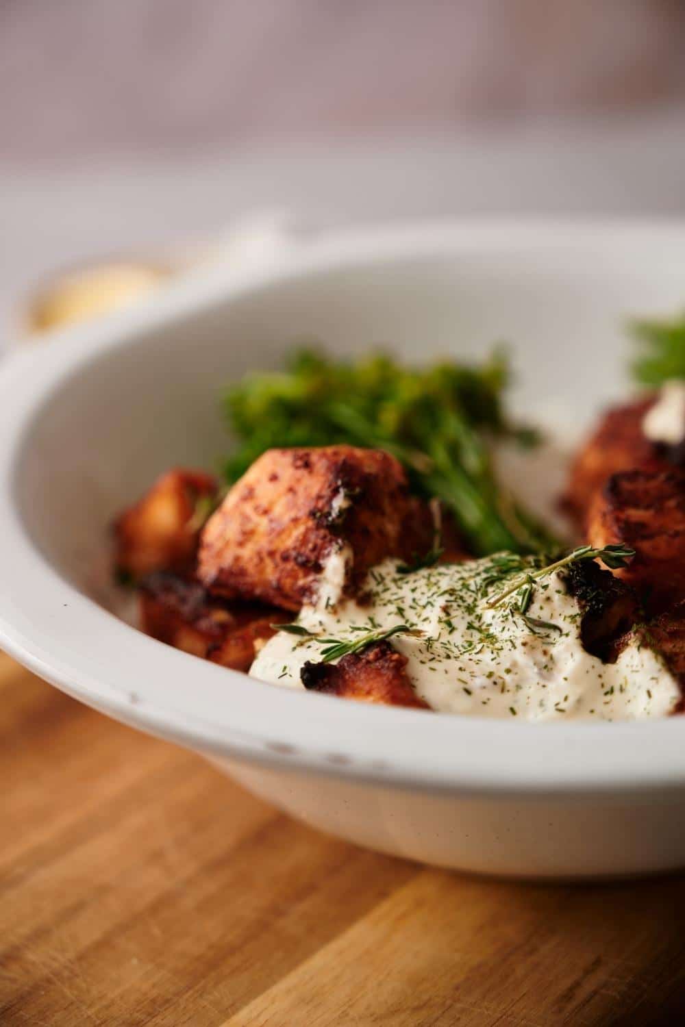 A close up of air fryer salmon bites served in a rice bowl. The salmon is topped with creamy dill sauce garnished with fresh chopped dill.