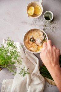 A hand mixing the bowl of dill sauce ingredients together.