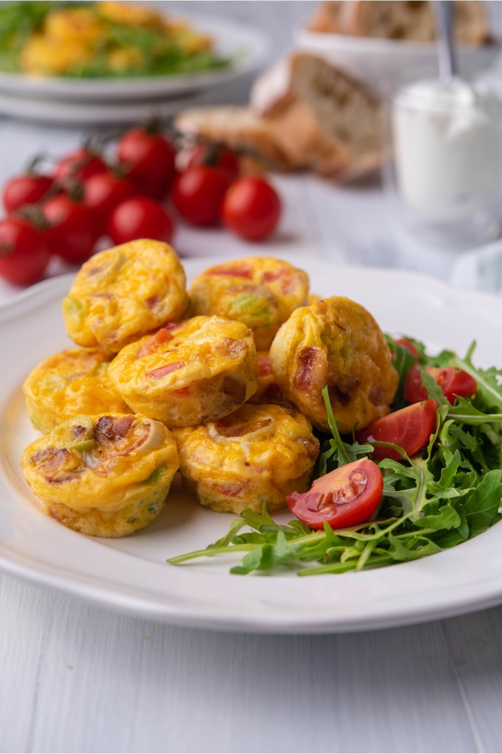 Several egg bites on top of one another on a plate with arugula and tomato.