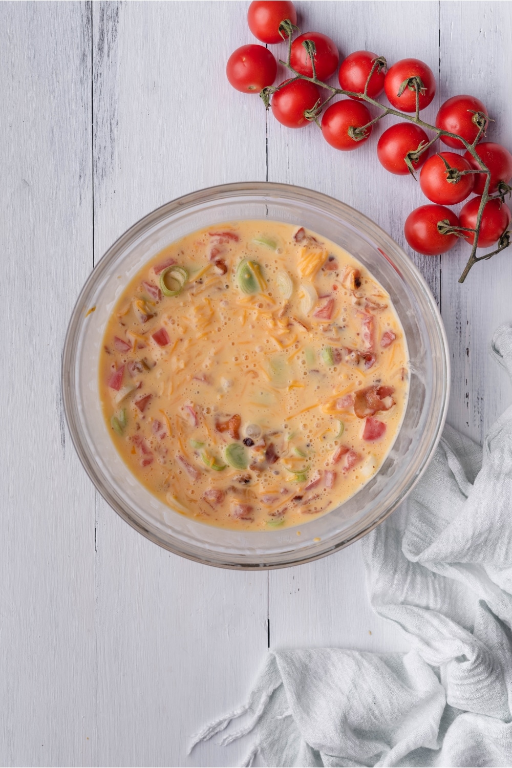 A bowl that is filled with whisked egg, tomato, onion, and cheese mixed together.