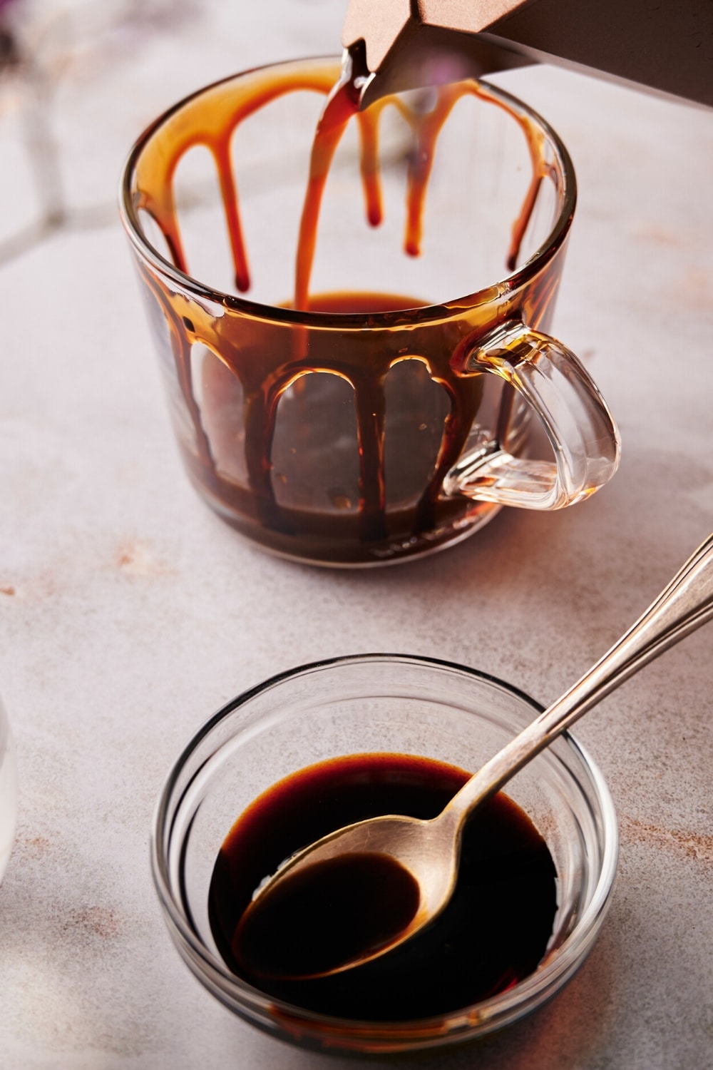 Espresso being poured into a glass that has caramel around it. In front of it is a bowl of caramel sauce with a spoon in it.