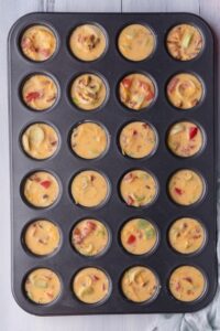 A mini muffin tray that is filled with uncooked mini egg bites