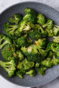 A bunch of broccoli florets sautéing in a pan.